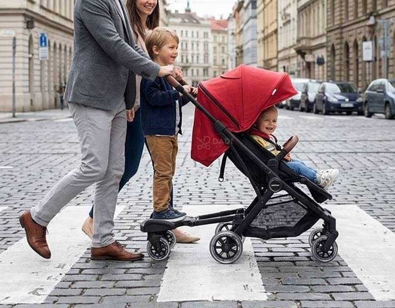 Starsze dziecko korzysta z buggy board podczas spaceru z wózkiem w miejskim otoczeniu.